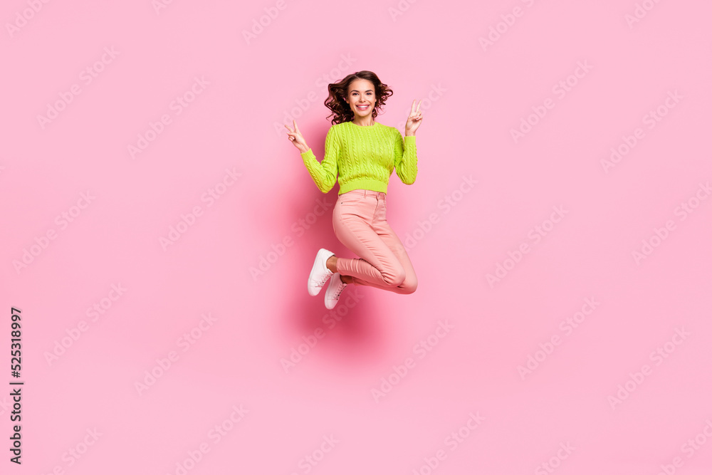 Full length photo of funny millennial lady jump show v-sign wear green shirt trousers shoes isolated on pink color background Full length photo of funny millennial lady jump show v-sign wear green shirt trousers shoes isolated on pink color background