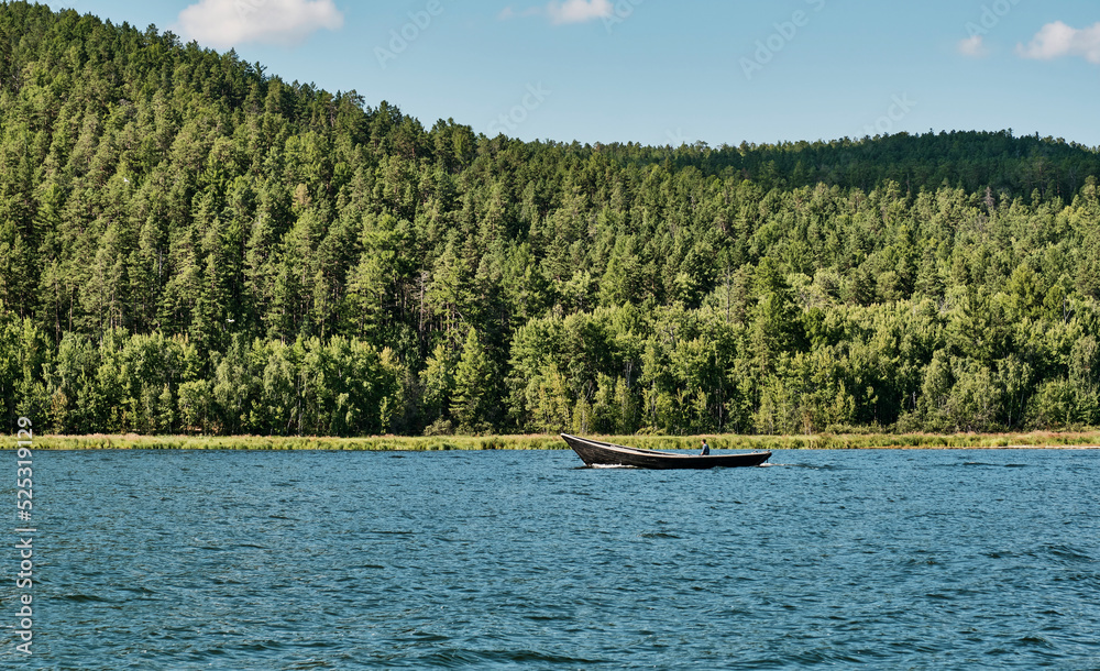 Man floating on fishing wooden longboat with motor along Chivyrkuisky Bay of Lake Baikal, Russia.
