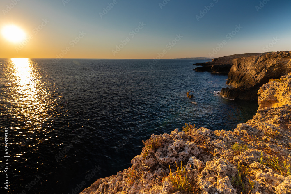 Amazing sunrise over the rising cliffs and rocks at Mellieha in the north west of Malta, with spectacular colors in the sky and reflections of the sun in het Mediterranean sea