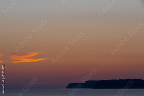 A colourful sunset over the cliffs of Paradis bay in Malta with a view on the Island of Gozo in the Mediterranean Sea. In summer the countries around the Mediterranean enjoy every evening these sunset