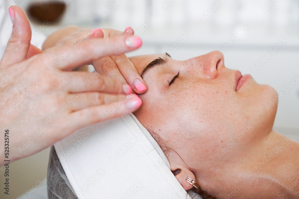 Fototapeta premium Pretty yanog woman receiving face massage, closeup photo. Beauty and health procedures in a beauty salon