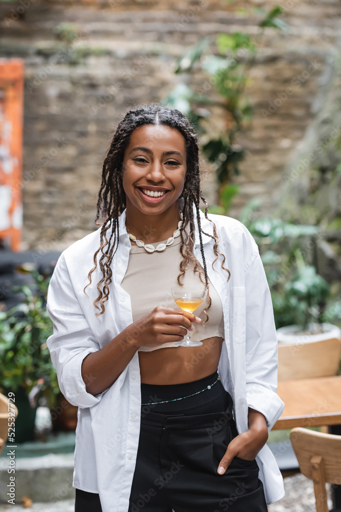 Positive african american woman holding glass of cocktail on terrace of cafe Positive african american woman holding glass of cocktail on terrace of cafe