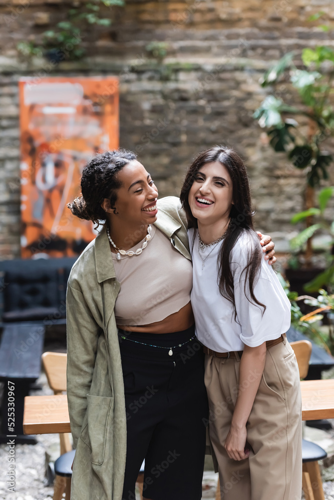 Cheerful african american woman hugging friend on terrace of cafe Cheerful african american woman hugging friend on terrace of cafe