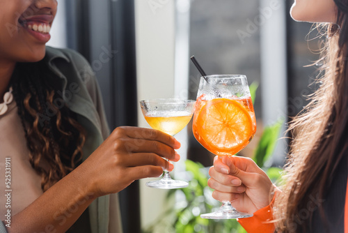 Cropped view of multiethnic girlfriends clinking cocktails in cafe