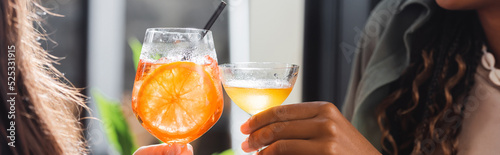 Εκτύπωση καμβά Cropped view of multiethnic girlfriends clinking cocktails in cafe, banner