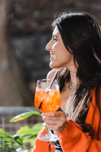 Side view of smiling woman holding blurred cocktail in cafe