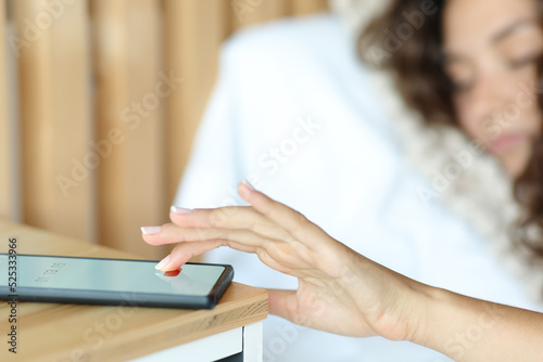 Sleepy woman stopping alarm on smart phone on a bed