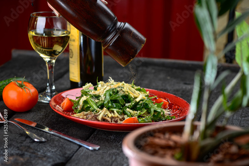 salad with meat, cheese, arugula and tomatoes in a red plate, macro photo sprinkled with pepper
