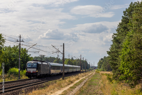 Nowoczesna czarna lokomotywa elektryczna z pociągiem międzynarodowym pędzi przez las