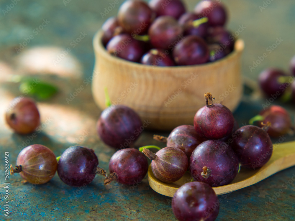 Obraz premium Gooseberries in a bowl on an old surface. leaves and berries of red and green gooseberries. Collect gooseberries. country style.