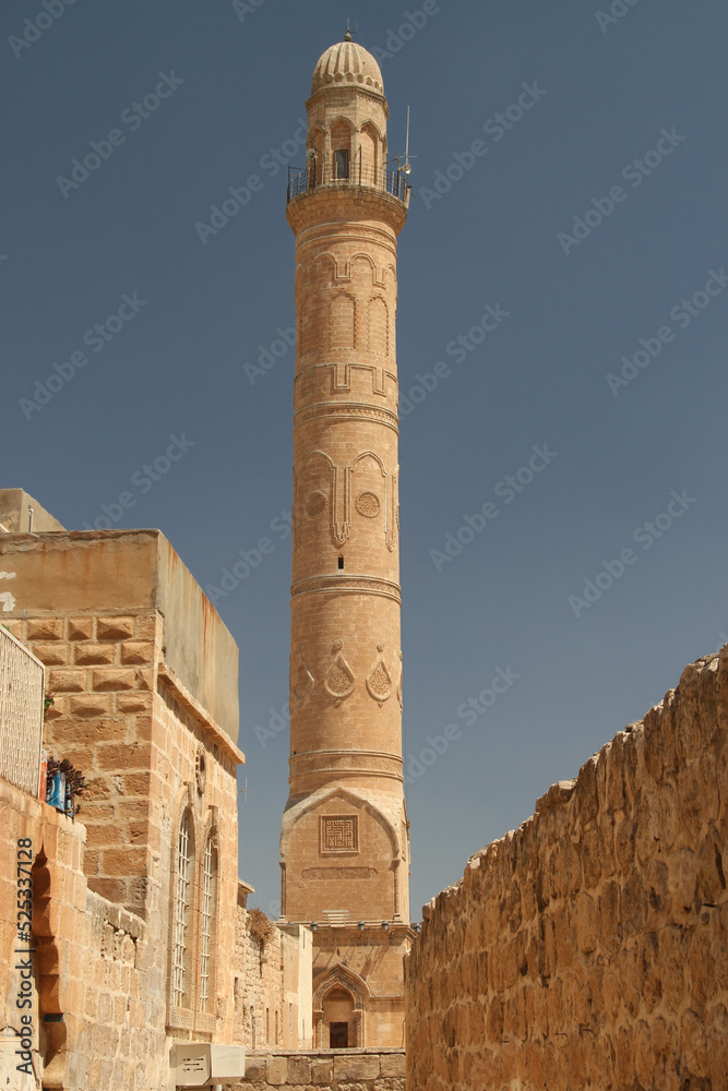 Obraz premium A view of the high ornate minaret of the Mardin Grand Mosque from a narrow street in the historic part of the city of Mardin in the Southeast Anatolia region of Turkey
