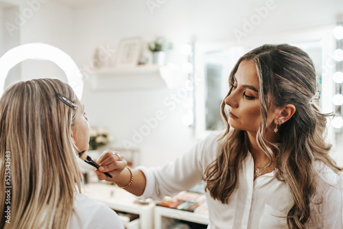 Makeup process. Professional artist applying make up on model face. Close up portrait of beautiful blonde woman in beauty saloon.