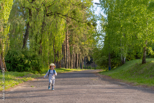 Wallpaper Mural a little girl in a yellow panama with a backpack runs along the path in the middle of the forest in sunny summer weather, the child enjoys rest on the background of greenery Torontodigital.ca