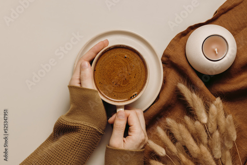 Hands with cup of coffee, linen cloth, dry lagurus grass and candle. Top view, flat lay, aesthetic minimal concept, brown tones
