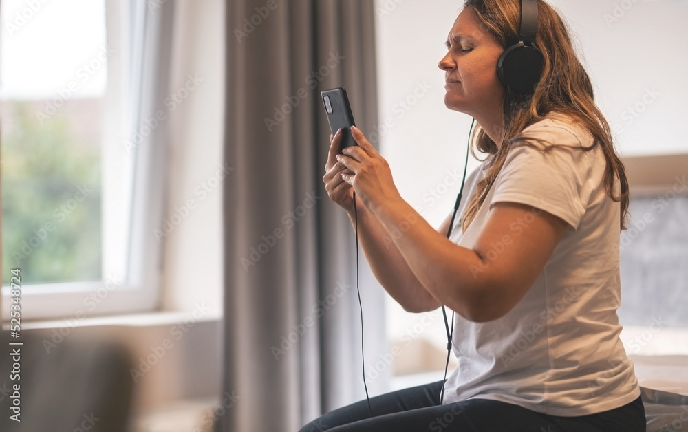 A woman with headphones on her ears emotionally enjoys music in her room. A woman with headphones on her ears emotionally enjoys music in her room.
