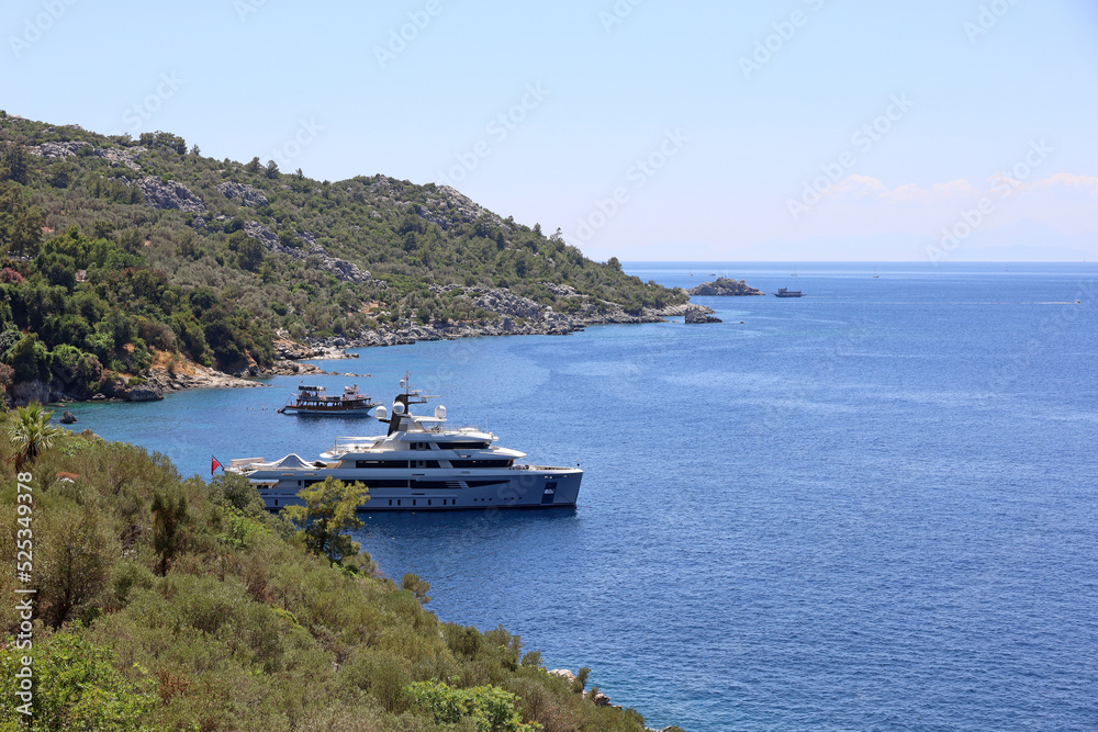 View to sea bay in Mediterranean sea with yachts and swimming people. Coast of Turkey with green mountains, summer tourism