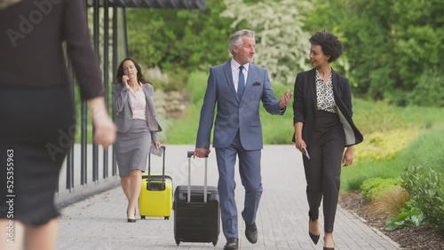 Group of business delegates with luggage arriving at conference hotel walking towards camera and talking - shot in slow motion