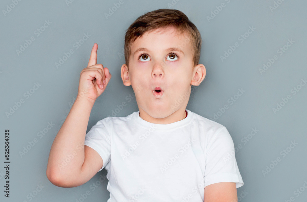 European handsome little boy is surprised, inspired, i have an idea, raise your index finger up, copy space, isolated on gray background. schoolboy European handsome little boy is surprised, inspired, i have an idea, raise your index finger up, copy space, isolated on gray background. schoolboy