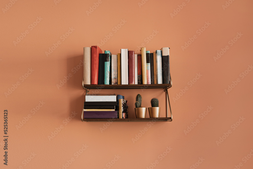 Books stack on hanging shelf. Coral peach wall background. Aesthetic minimal interior design. Reading, education concept with bookshelf Books stack on hanging shelf. Coral peach wall background. Aesthetic minimal interior design. Reading, education concept with bookshelf
