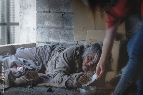 Homeless beggar man sleeps in a corner of a building near the pedestrian walkway, someone brought him a dollar bill