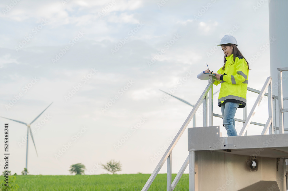 women engineer working and holding the report at wind turbine farm Power Generator Station on mountain,Thailand people