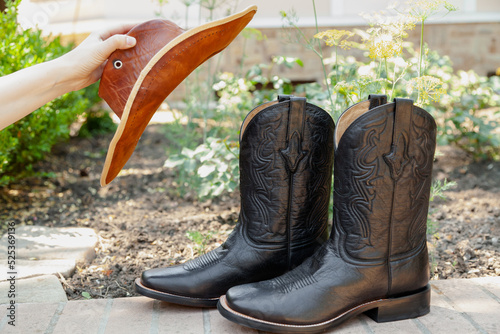 Photography woman hand holds leather hat in front of cowboy boots....
