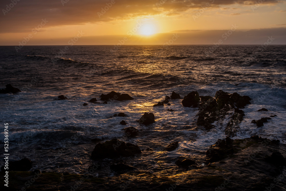 puesta de sol en la playa con un mar con olas rompiendo en las rocas de la costa