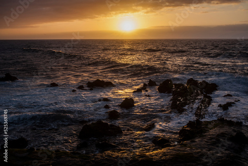 puesta de sol en la playa con un mar con olas rompiendo en las rocas de la costa photo