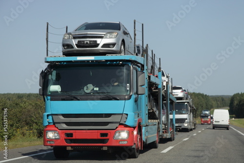 Loaded two level used car carrier trucks with car transporter semi trailers drive on suburban highway road at summer day. Front side view close up. Delivery autos logistics. Automobile transportation