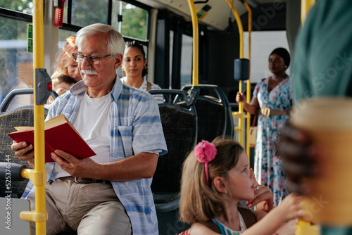 Senior man reading book on city bus