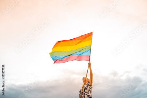 Senior woman waving rainbow flag outdoors at sunset
