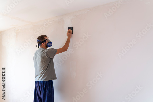 Fotografie Man sanding wall with sandpaper. Title space at frame.