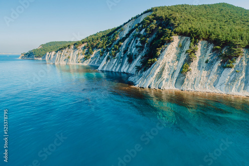 Aerial view of scenic coastline with blue sea and cliffs with forest. Summer day on sea