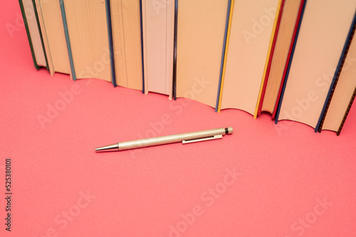 Books on pink background with silver pen writing a book photo