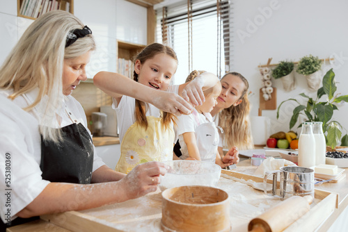 Happy grandchild breaking egg into bowl before kneading dough baking cooking cookies biscuits. Delighted granny watching process managing. Mom with preschholer daughter talking.