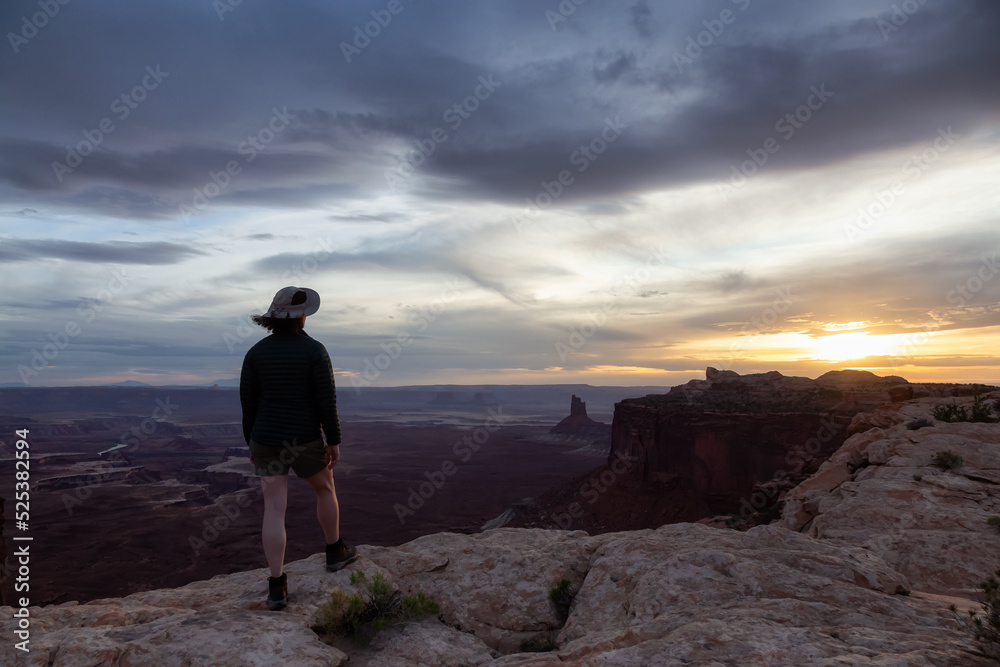 Adventurous Woman Hiking at a Desert Canyon with Red Rock Mountains. Cloudy Sunset Sky. Canyonlands National Park. Utah, United States. Adventure Travel Adventurous Woman Hiking at a Desert Canyon with Red Rock Mountains. Cloudy Sunset Sky. Canyonlands National Park. Utah, United States. Adventure Travel