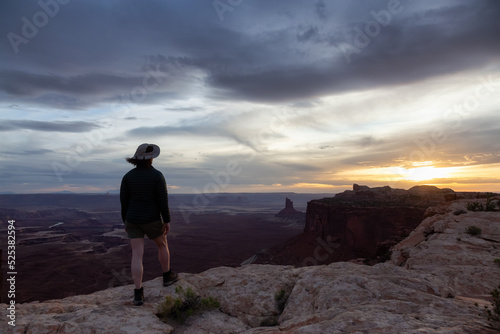 Adventurous Woman Hiking at a Desert Canyon with Red Rock Mountains. Cloudy Sunset Sky. Canyonlands National Park. Utah, United States. Adventure Travel © edb3_16