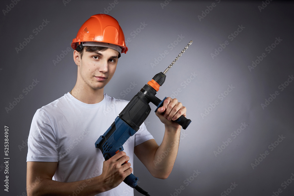 a young construction worker in a hard hat and a white T-shirt with a puncher in his hand. a young construction worker in a hard hat and a white T-shirt with a puncher in his hand.