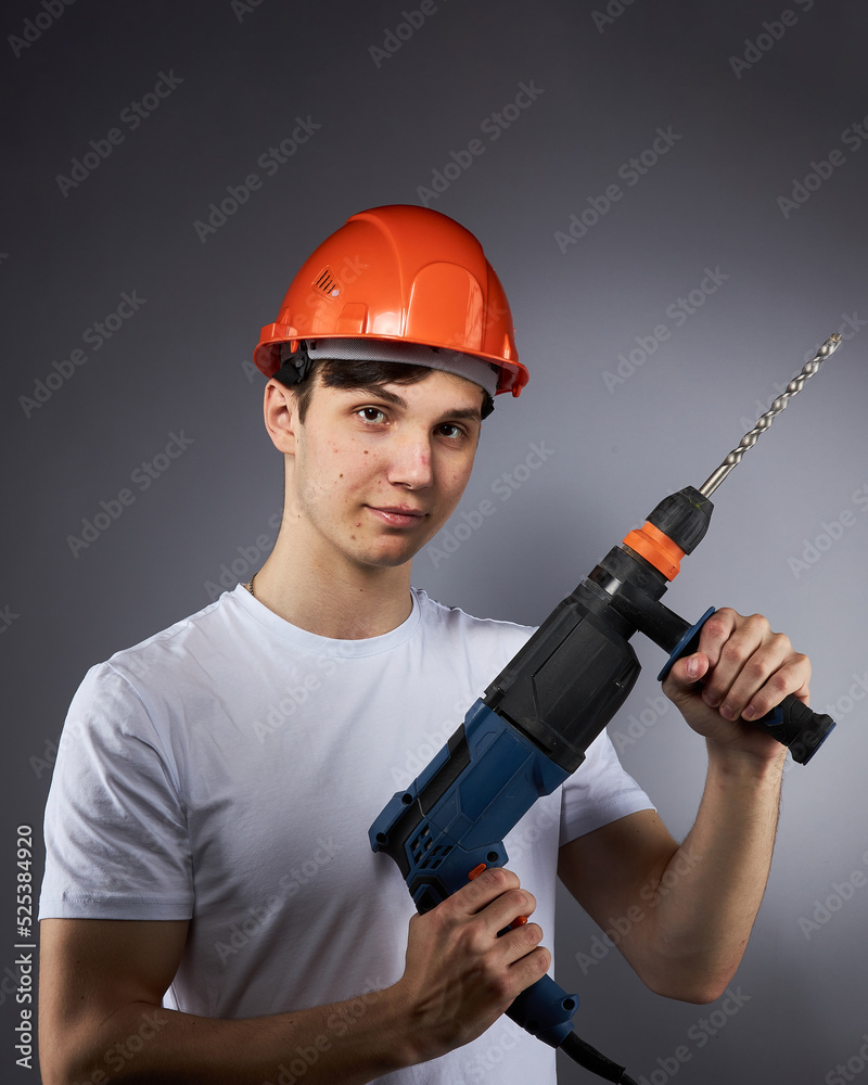 a young construction worker in a hard hat and a white T-shirt with a puncher in his hand. a young construction worker in a hard hat and a white T-shirt with a puncher in his hand.