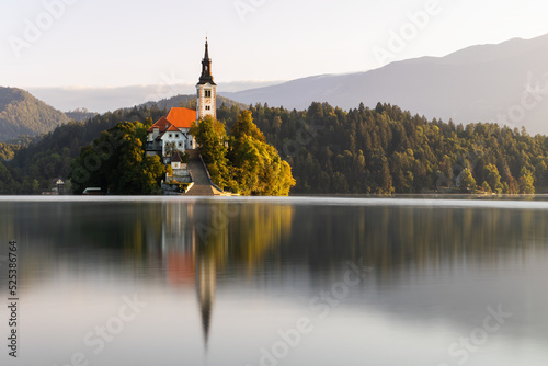 A church in the middle of an Bled lake in Slovenia at sunrise. Tourist destination with historic building set into lovely nature surrounding with reflection on water surface. photo