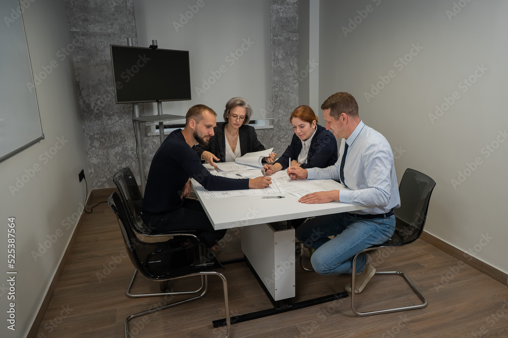 Four colleagues are discussing blueprints in a conference room in an office. Brainstorming of engineers and architects. Four colleagues are discussing blueprints in a conference room in an office. Brainstorming of engineers and architects.
