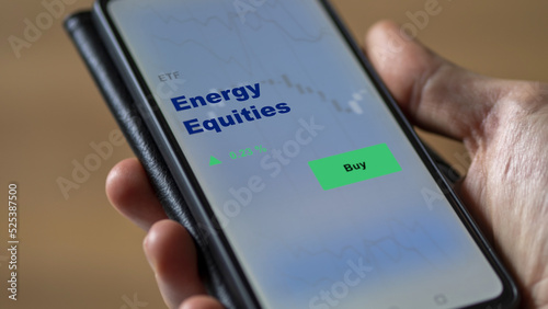 An investor's analyzing the energy equities etf fund on screen. A phone shows the ETF's prices energy equity to invest