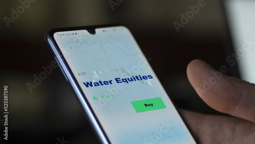 An investor's analyzing the water equities etf fund on screen. A phone shows the ETF's prices stocks to invest