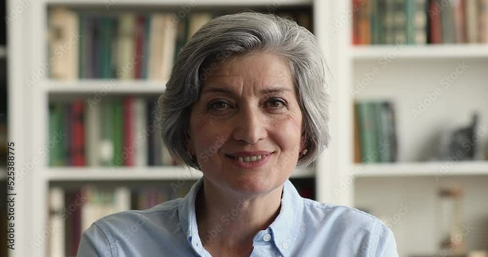Senior older grey haired Latin woman posing with serious and happy face, looking and camera with toothy smile, showing positive emotion, giving reaction to good news. Indoor headshot portrait