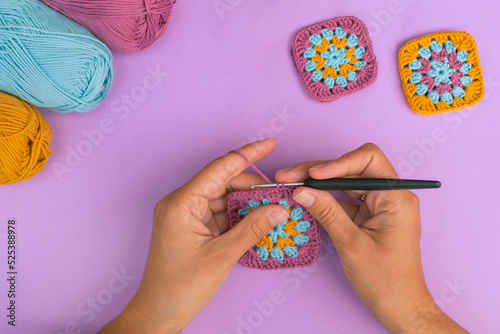 Photography Top view of wonan's hands crocheting multicolored granny square with skeins of c