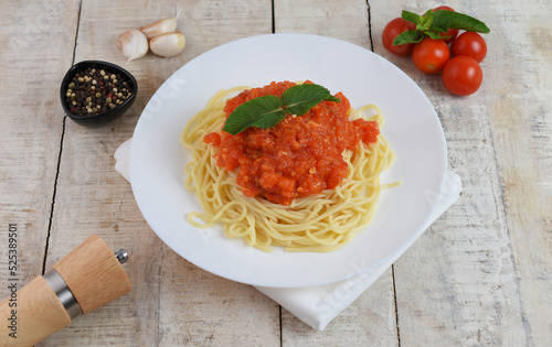 Spaghetti or pasta with tomato sauce and fresh green basil on a white plate with cherry tomato on wooden table