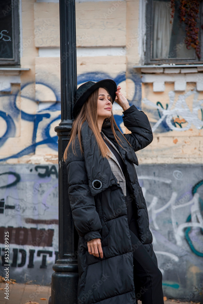 romantic beautiful brunette smiling girl in a black hat walking in the autumn city