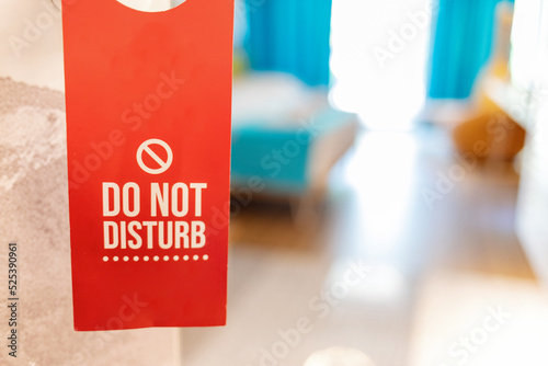 ''Do not disturb'' sign on a handle of hotel room door with bed in the background. Hotel door handle with a do not disturb sign request.