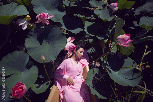 portrait beautiful brunette woman in a pink dress is lies on a boat among blooming lotuses on a lake in Astrakhan.