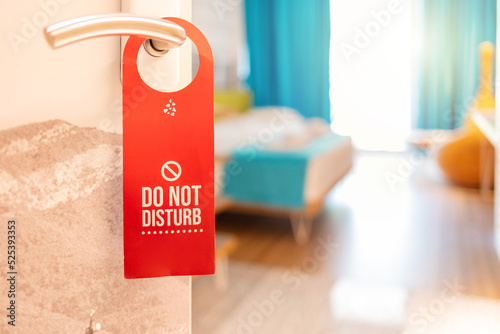 "Do not disturb" plate sign which is hanging on the door handle. Close-up at the object, selective focus at partial part of the text. Sign on the door do not disturb in hotel.